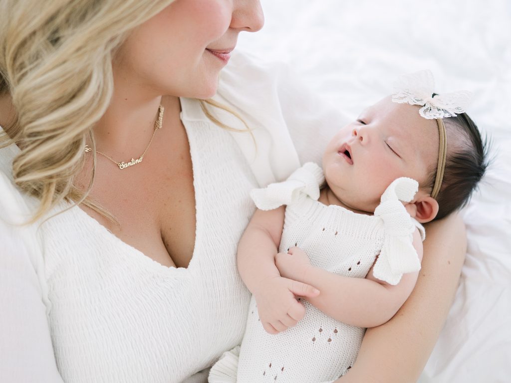 Mom holding baby girl in white with a bow for newborn photography session